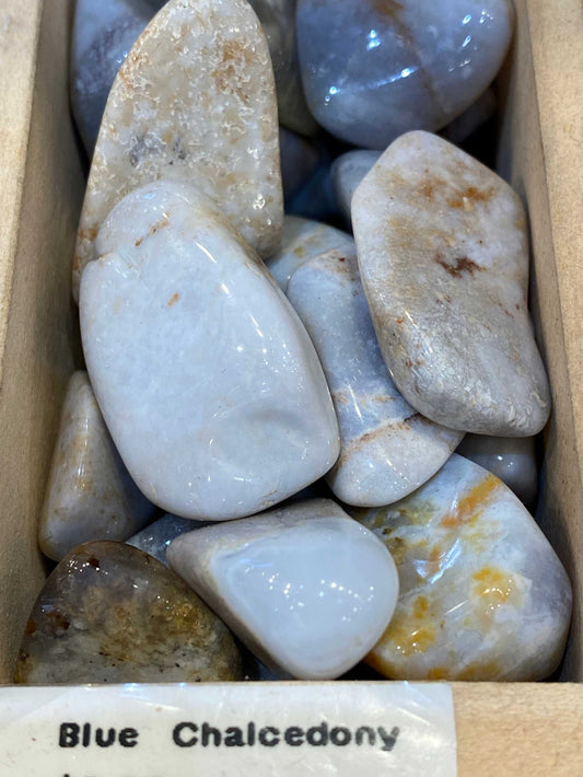 Blue Chalcedony tumbled stones in a wooden box showcasing their smooth surface and natural patterns.