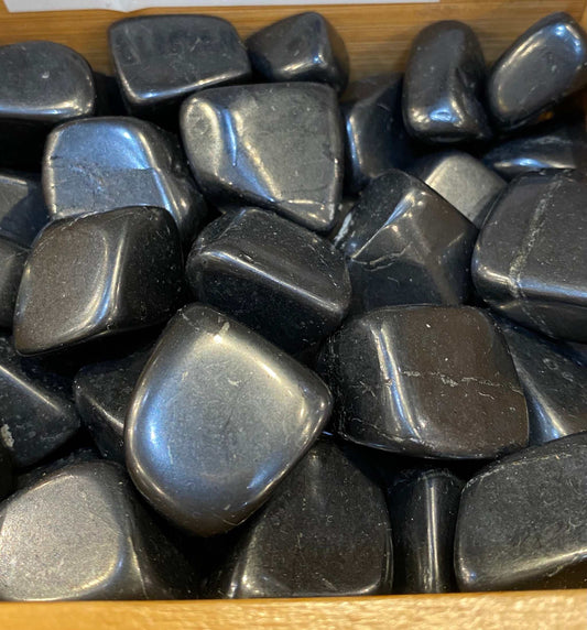 Shungite tumbled stones in a wooden tray for balance and well-being.