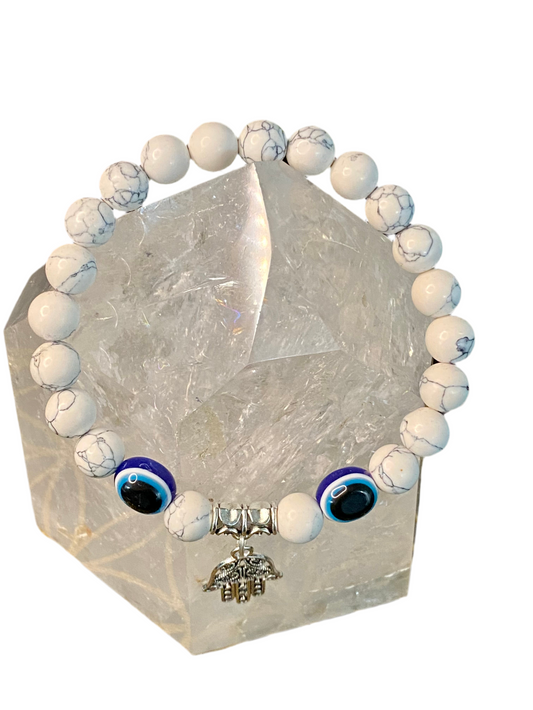 Howlite Evil Eye Gemstone Bracelet with Hamsa Charm on clear crystal stand.