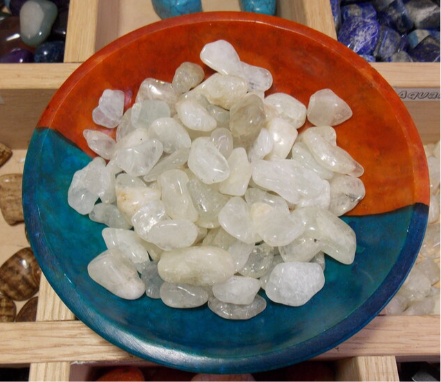 Aquamarine tumbled stones in a colorful dish, promoting serenity and emotional healing.