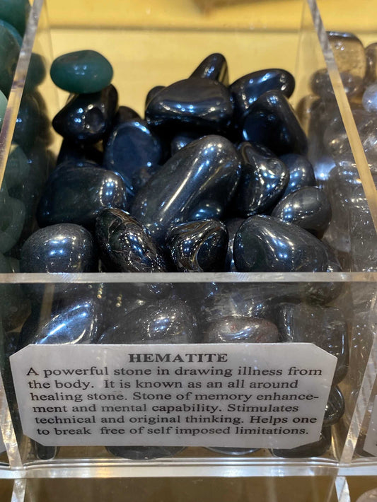 Hematite tumbled stones in a display box, showcasing their polished, reflective gray surface.