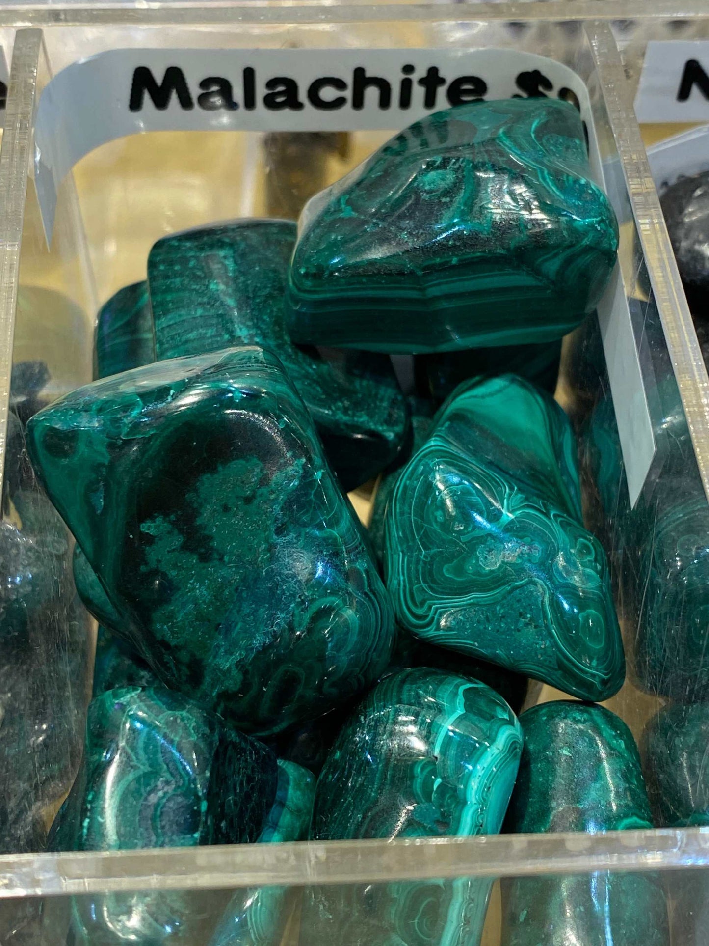Malachite Crystal Tumbled Stones with green hues in a display box, enhancing spiritual insight and emotional healing.