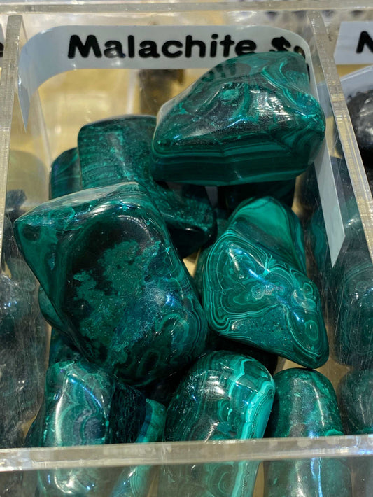 Malachite Crystal Tumbled Stones with green hues in a display box, enhancing spiritual insight and emotional healing.