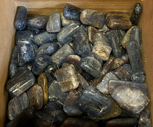 Blue Kyanite tumbled stones displayed in a wooden box for promoting loyalty, honesty, and peace.