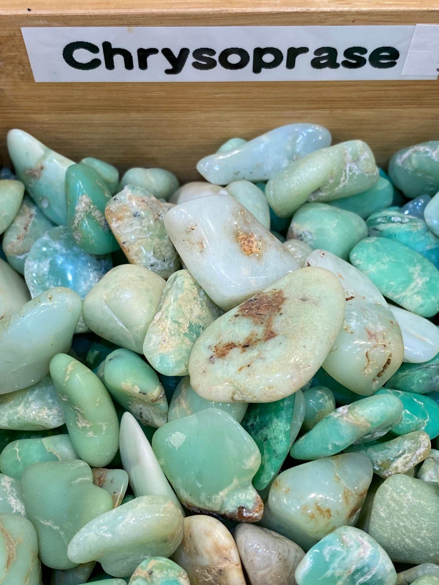 Chrysoprase tumbled stones in various shades of green displayed in a wooden box.