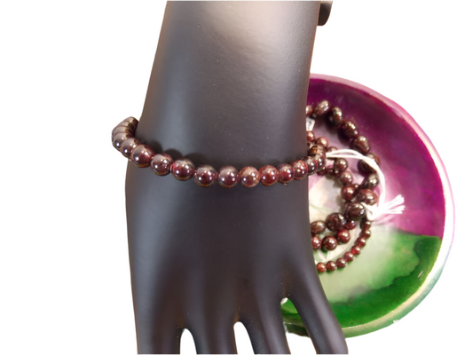 Red Garnet Bracelet on a mannequin hand over a colorful dish background.