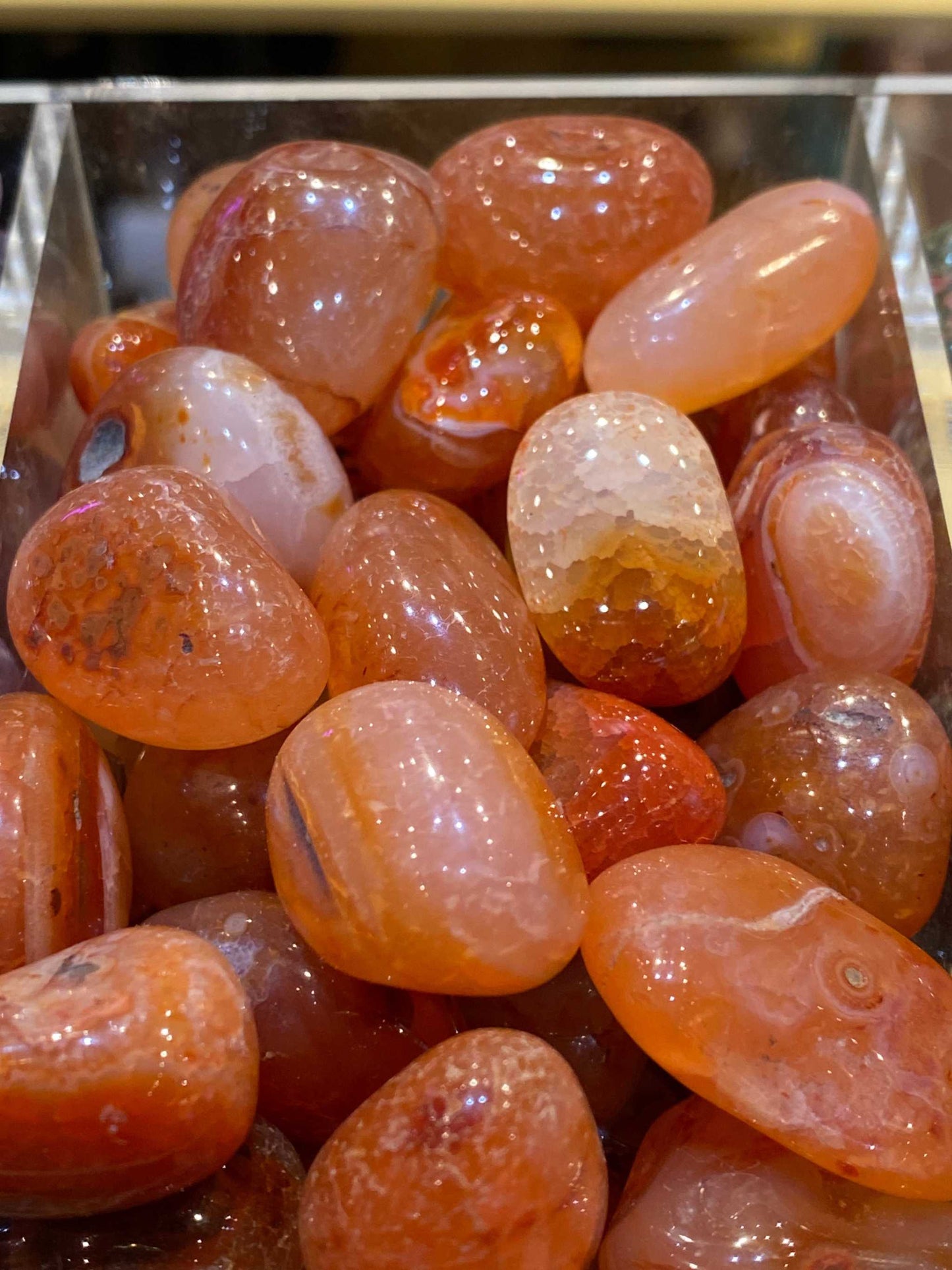 Tumbled polished Carnelian stones displayed in a metal container.