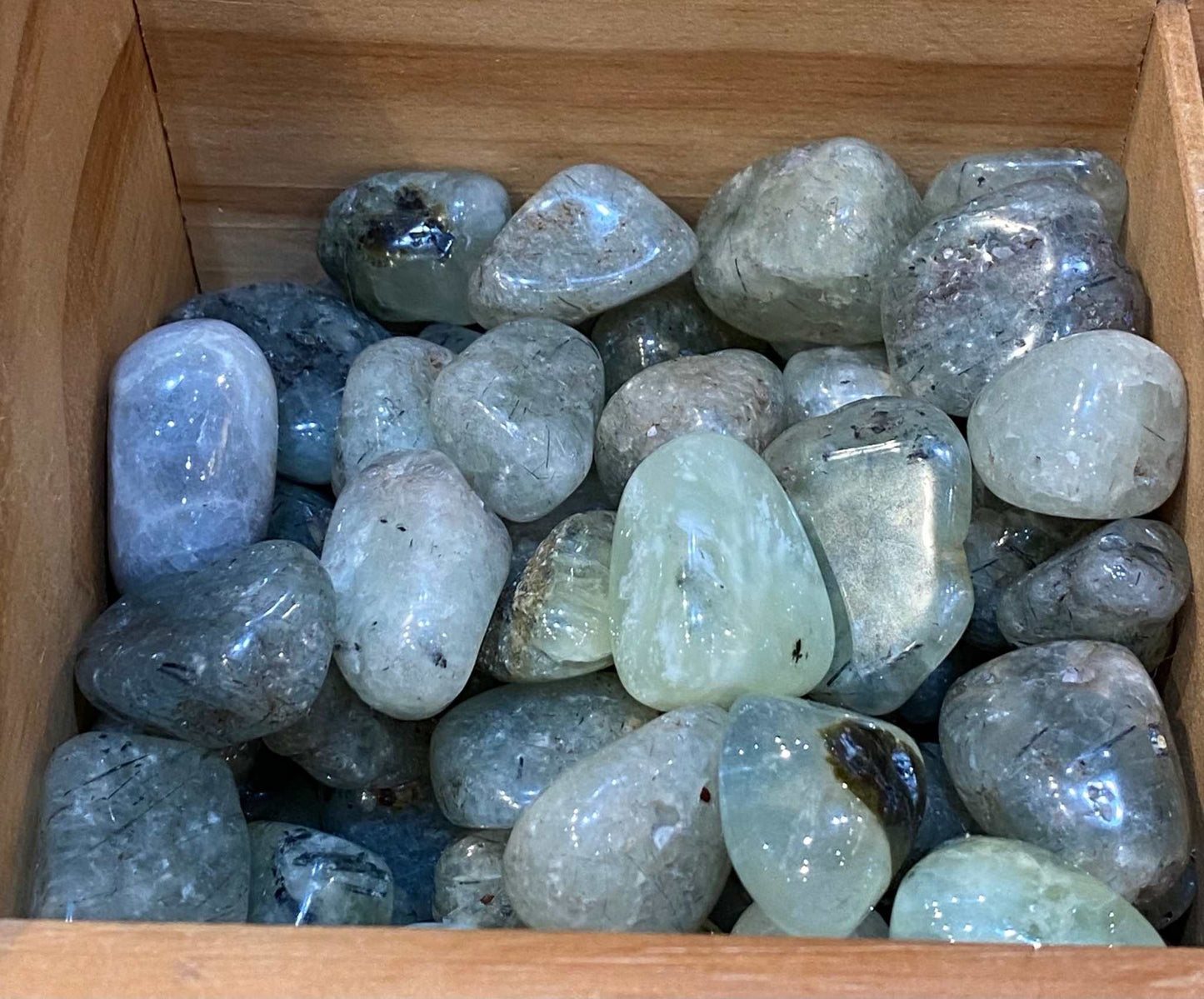 Prehnite and Epidote tumbled stones in a wooden box, promoting psychic awareness and self-care.