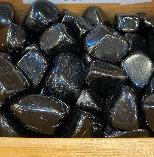 Jet Tumbled Stones in a wooden box, showcasing smooth black surfaces and glossy finish. Ideal for grounding, protection, and Capricorn energy connection.