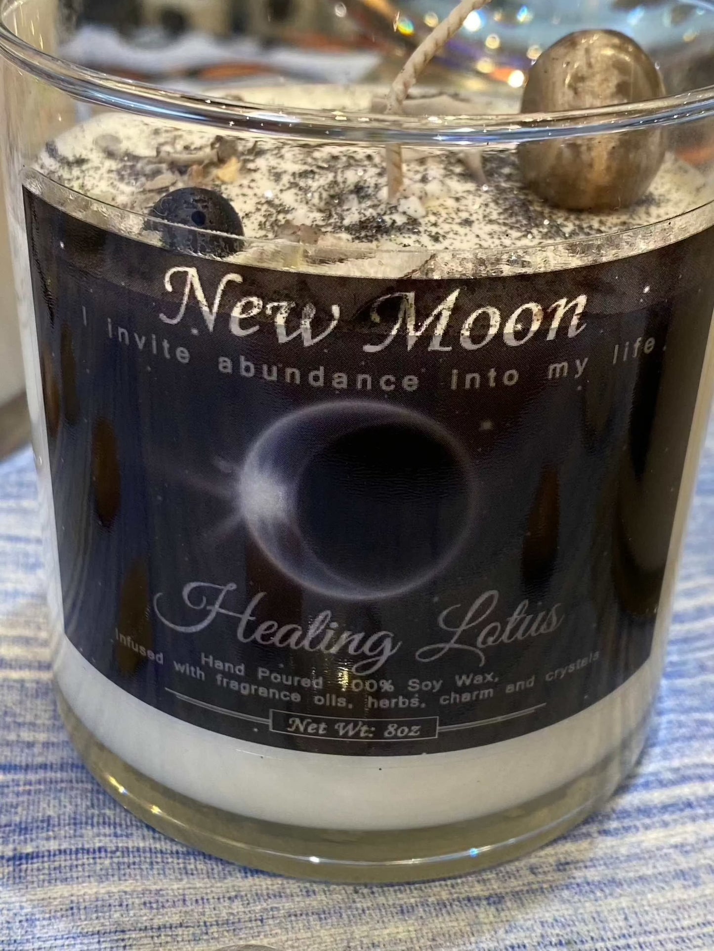 New Moon Candle by Healing Lotus set on a table, featuring crystals and herbs for abundance and new beginnings.